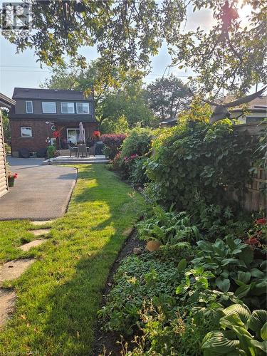 Expansive backyard featuring a manicured lawn, established garden beds with diverse foliage, a paved patio area, and a red brick exterior with a second-story dormer - 851 Beach Boulevard, Hamilton, ON - Outdoor With Deck Patio Veranda