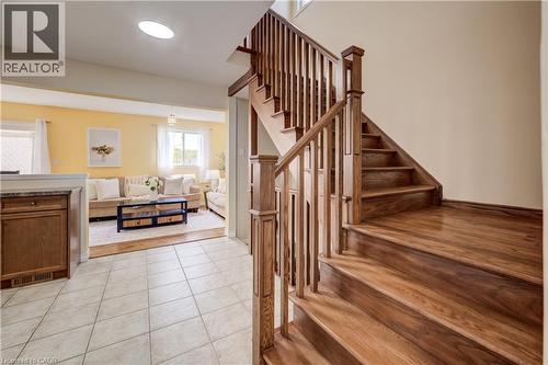 Hardwood staircase with natural wood railings, offering a visual separation from the living area with light yellow walls and multiple windows - 124 Prosperity Drive, Kitchener, ON - Indoor Photo Showing Other Room