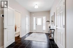 Entry foyer featuring dark square floor tiles, a white front door with decorative glass inserts, and an overhead flush-mount light fixture - 