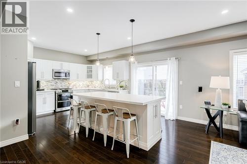 Kitchen featuring white cabinetry, stainless steel appliances, a tile backsplash, and a central island with countertop seating - 7 Kinsman Drive, Binbrook, ON - Indoor