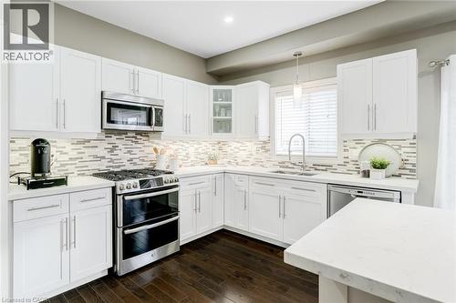 Modern kitchen featuring white cabinetry, light countertops, stainless steel appliances, a tile backsplash, and dark wood-finish flooring - 7 Kinsman Drive, Binbrook, ON - Indoor Photo Showing Kitchen With Upgraded Kitchen