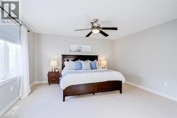 Spacious bedroom featuring light-colored carpet flooring, a large window with blinds and sheer curtains, and a ceiling fan with integrated lighting - 