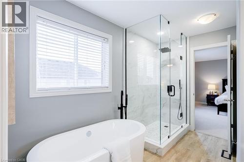 Freestanding soaking tub with matte black floor-mounted faucet, glass-enclosed shower featuring marble-look tile, and wood-finish flooring - 7 Kinsman Drive, Binbrook, ON - Indoor Photo Showing Bathroom