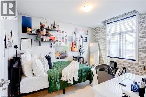 Bedroom featuring a large window with blinds, a white brick-patterned accent wall, and built-in wall shelving - 7 Kinsman Drive, Binbrook, ON - Indoor