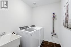 Dedicated laundry area featuring a utility sink with dual-handle faucet, top-load washing machine, front-load dryer, and dark square tile flooring - 