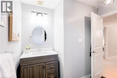 Powder room featuring a wood-finish vanity with drawer and cabinet storage, a white countertop with an integrated sink, and an oval mirror - 7 Kinsman Drive, Binbrook, ON - Indoor Photo Showing Bathroom