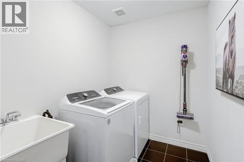 Dedicated laundry area featuring a utility sink with dual-handle faucet, top-load washing machine, front-load dryer, and dark square tile flooring - 7 Kinsman Drive, Binbrook, ON - Indoor Photo Showing Laundry Room