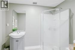 Bathroom featuring a glass-enclosed shower, a vanity with a white ceramic sink, a rectangular wall-mounted mirror, and light-toned walls - 