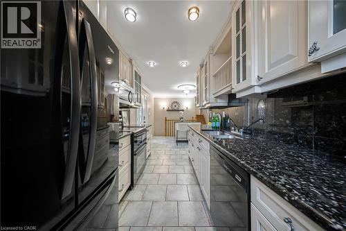 Galley kitchen featuring cream cabinetry with glass-front uppers, black stone countertops, tile flooring, and recessed lighting - 124 Dunsmere Drive, Kitchener, ON - Indoor Photo Showing Kitchen With Double Sink With Upgraded Kitchen