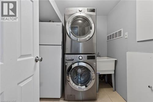 Laundry area featuring stacked stainless steel washer and dryer, utility sink with chrome faucet, and light gray wall paint - 1172 Chada Avenue, Mississauga, ON - Indoor Photo Showing Laundry Room