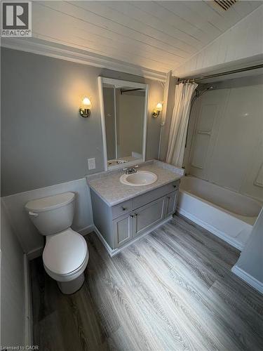 Bathroom featuring a single vanity with a surface-mounted sink, built-in cabinetry, overhead wall sconces, and wood-finish flooring - 104 Marshall Street, Waterloo, ON - Indoor Photo Showing Bathroom