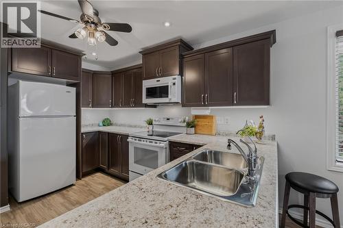 Kitchen featuring dark wood-finish cabinetry, light speckled countertops, and a white tile backsplash - 51 Millcroft Drive, Simcoe, ON - Indoor Photo Showing Kitchen With Double Sink