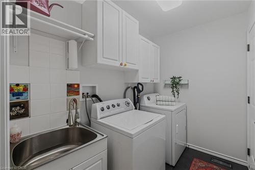 Dedicated laundry space featuring white cabinetry, a utility sink with a pull-down faucet, and white tile backsplash - 51 Millcroft Drive, Simcoe, ON - Indoor Photo Showing Laundry Room