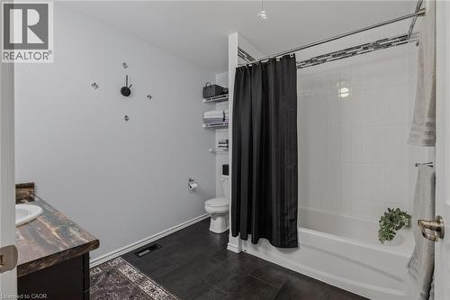 Bathroom featuring a full tub with white subway tile surround, dark wood-finish flooring, and a single vanity with a patterned countertop - 51 Millcroft Drive, Simcoe, ON - Indoor Photo Showing Bathroom