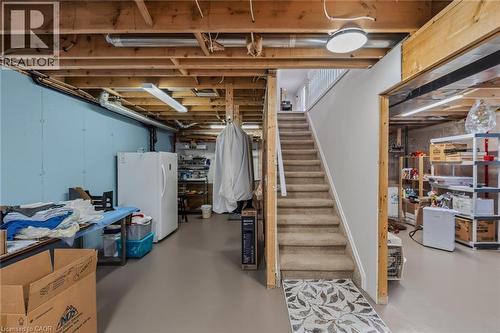 Unfinished basement space featuring exposed wood joists and structural beams, a carpeted staircase with white railings, and painted foundation walls - 51 Millcroft Drive, Simcoe, ON - Indoor Photo Showing Basement