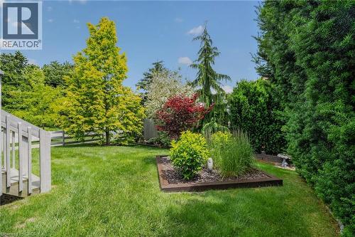 Expansive lawn area featuring a raised garden bed with established plantings, mature trees, a privacy hedge, and a partial wood fence - 51 Millcroft Drive, Simcoe, ON - Outdoor