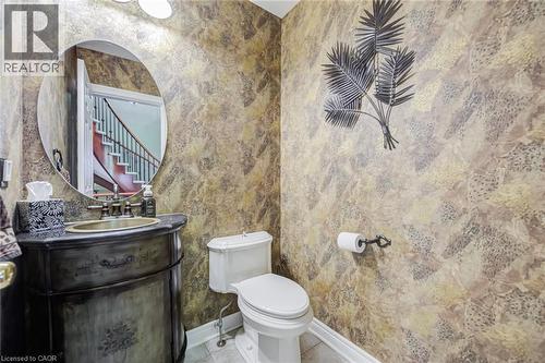 Powder room featuring decorative wall covering, a dark wood-finish vanity with an integrated sink, an oval wall mirror, and a white toilet - 4278 Clubview Drive, Burlington, ON - Indoor Photo Showing Bathroom