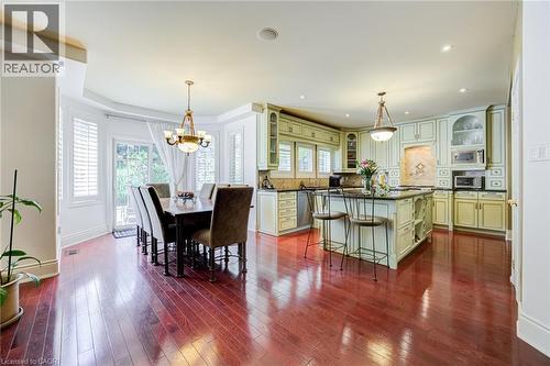 Expansive kitchen and dining area featuring rich wood-finish flooring, light-toned cabinetry, a central kitchen island with seating, a patterned tile backsplash, and recessed lighting - 4278 Clubview Drive, Burlington, ON - Indoor Photo Showing Dining Room