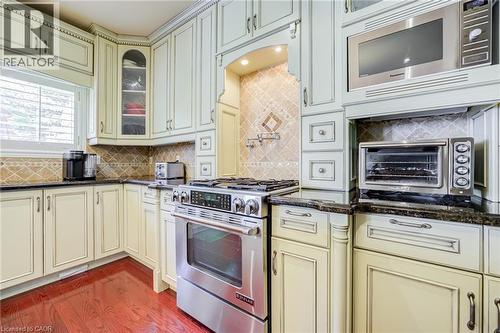 Custom cabinetry with an antiqued finish, stone countertops, stainless steel range, built-in microwave, and wood-finish flooring - 4278 Clubview Drive, Burlington, ON - Indoor Photo Showing Kitchen