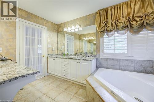 Bathroom featuring a built-in tub with tile surround, dual vanity with granite countertop, and tile flooring - 4278 Clubview Drive, Burlington, ON - Indoor Photo Showing Bathroom