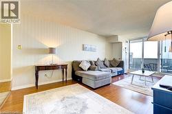 Spacious living area featuring wood-finish flooring, a wall of vertical stripe wallpaper, and sliding glass doors leading to a private outdoor balcony - 