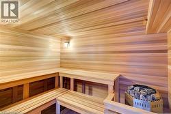 Interior sauna featuring light wood paneling, multi-level wood benches, a built-in wall light fixture, and a rock-filled heater unit - 