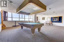 Recreation room featuring a full-size billiards table with overhead lighting, patterned carpet flooring, and a wall of windows - 