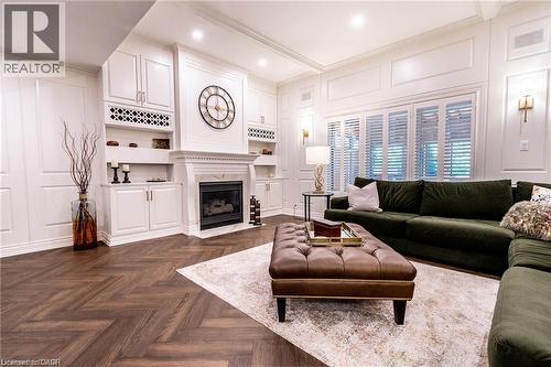 Living area featuring a herringbone wood-finish floor, built-in cabinetry, an integrated fireplace, decorative wall paneling, and interior window shutters - 76 Adriatic Boulevard, Hamilton, ON - Indoor Photo Showing Living Room With Fireplace