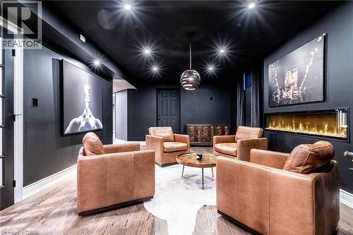Media room featuring dark wall and ceiling finishes, recessed lighting, a linear electric fireplace, wood-finish flooring, and a pendant light fixture - 76 Adriatic Boulevard, Hamilton, ON - Indoor