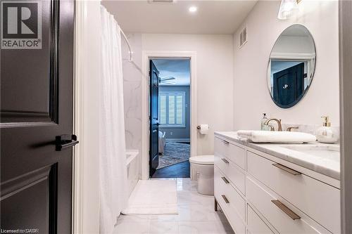 Contemporary bathroom featuring a spacious vanity with a stone countertop, an oval mirror, and a built-in shower with white tile surround - 76 Adriatic Boulevard, Hamilton, ON - Indoor Photo Showing Bathroom