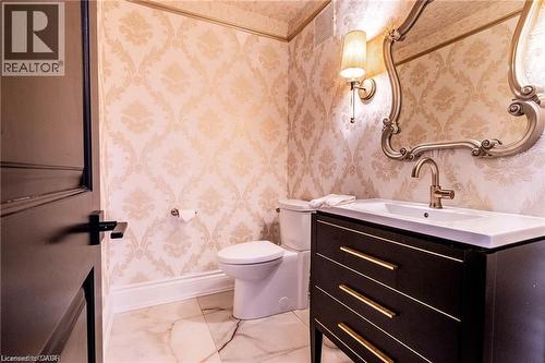 Powder room featuring ornamental wallpaper, a dark wood vanity with gold-tone hardware, a modern vessel sink, and a matching gold-tone faucet - 76 Adriatic Boulevard, Hamilton, ON - Indoor Photo Showing Bathroom