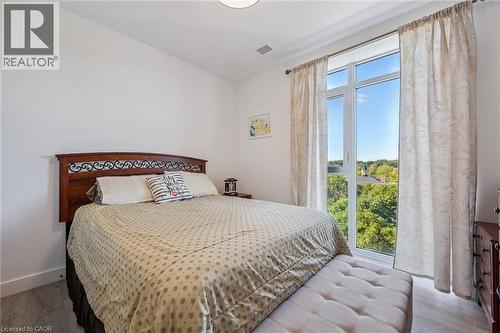 Floor-to-ceiling window with tree canopy scenery, light wood-finish flooring, white walls, and a decorative headboard - 15 Glebe Street Unit# 902, Cambridge, ON - Indoor Photo Showing Bedroom