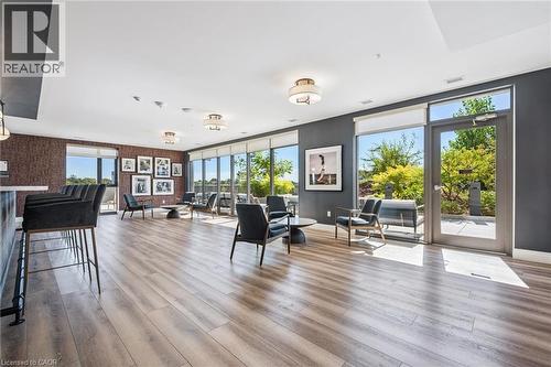 Spacious common area featuring wood-finish flooring, a built-in bar with pendant lighting, multiple large windows, and an outdoor patio access - 15 Glebe Street Unit# 902, Cambridge, ON - Indoor