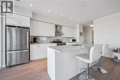 Modern kitchen featuring a large island with countertop seating, stainless steel appliances, white cabinetry, and wood-finish flooring - 15 Glebe Street Unit# 902, Cambridge, ON - Indoor Photo Showing Kitchen With Stainless Steel Kitchen With Double Sink With Upgraded Kitchen