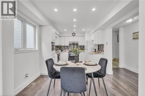 Open-concept kitchen and dining area featuring recessed lighting, wood-finish flooring, white cabinetry, stainless steel appliances, and a mosaic tile backsplash - 425 Erinbrook Drive, Kitchener, ON - Indoor Photo Showing Dining Room