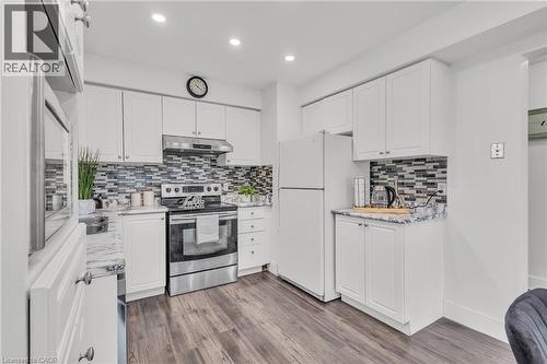 Kitchen with white cabinetry, stainless steel range and range hood, patterned tile backsplash, and wood-finish flooring - 425 Erinbrook Drive, Kitchener, ON - Indoor Photo Showing Kitchen With Upgraded Kitchen