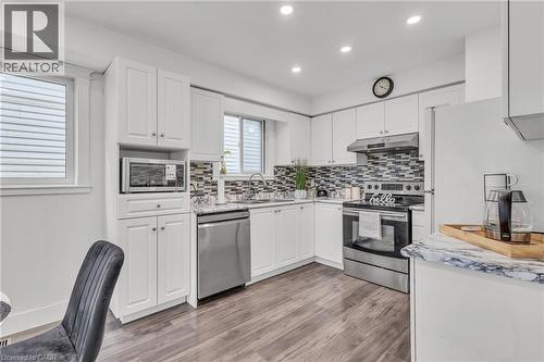 Modern kitchen featuring white shaker cabinetry, stainless steel appliances, a multi-tone tile backsplash, marbling countertops, and wood-finish flooring - 425 Erinbrook Drive, Kitchener, ON - Indoor Photo Showing Kitchen With Upgraded Kitchen
