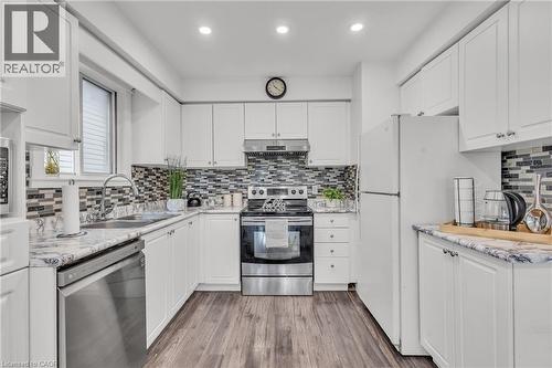 L-shaped kitchen featuring white cabinetry, a mosaic tile backsplash, wood-finish flooring, a stainless steel dishwasher, and a double basin sink with a gooseneck faucet - 425 Erinbrook Drive, Kitchener, ON - Indoor Photo Showing Kitchen With Double Sink With Upgraded Kitchen