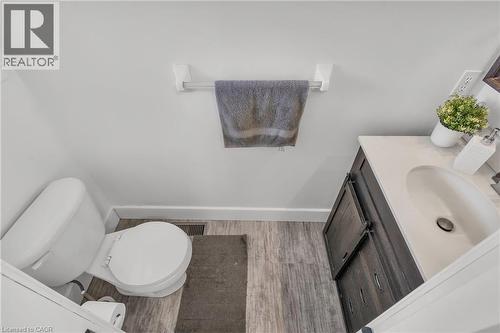 Bathroom featuring a white toilet, wood-finish flooring, a dark wood-finish vanity with a white countertop, and an oval sink with a chrome faucet - 425 Erinbrook Drive, Kitchener, ON - Indoor Photo Showing Bathroom