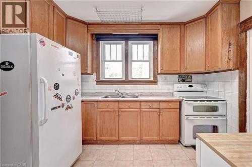 Kitchen featuring a double basin sink, white tile backsplash, wood-finish cabinetry, and neutral-toned floor tiling - 147 Courtland Avenue E, Kitchener, ON - Indoor Photo Showing Kitchen With Double Sink