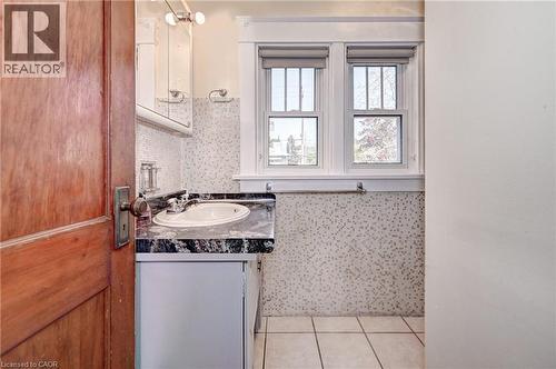 Compact bathroom featuring an integrated sink with a dark stone countertop, white vanity cabinetry, mosaic tile wainscoting, and a white tile floor - 147 Courtland Avenue E, Kitchener, ON - Indoor Photo Showing Bathroom