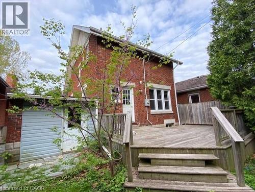 Rear brick elevation featuring a wooden deck with railing and steps, a side entry door, and a ground-level outbuilding with siding - 1066 Richmond Street, London, ON - Outdoor With Exterior