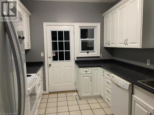 Galley kitchen featuring white cabinetry, dark countertops, white tile flooring, and a glass-paned exterior door - 1066 Richmond Street, London, ON - Indoor Photo Showing Kitchen