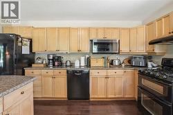 Kitchen featuring light wood cabinetry, dark wood-finish flooring, granite countertops, and stainless steel and black appliances - 