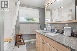 Bathroom featuring a single vanity with a granite-style countertop, undermount sink, and light wood-finish cabinetry - 