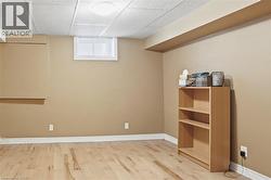 Finished basement space featuring light wood-finish flooring, neutral wall tones, white baseboards, and a dropped ceiling with recessed lighting - 