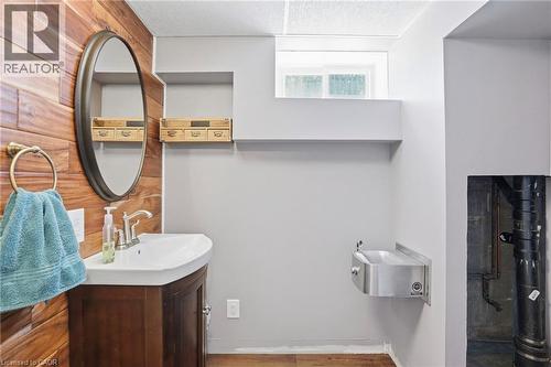 Powder room featuring a wood-panel accent wall, oval mirror, and a dark wood vanity with a white basin sink - 25 Saveryn Road, Hamilton, ON - Indoor Photo Showing Bathroom