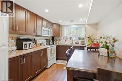Kitchen featuring wood-finish cabinetry, light-toned countertops, tile backsplash, and a window with blinds - 