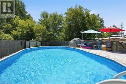 Outdoor swimming pool with integrated wood deck, complete with a surrounding privacy fence and mature perimeter trees - 