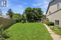 Expansive grassy yard with full fencing, mature perimeter trees, and a side pathway leading to a wooden gate - 